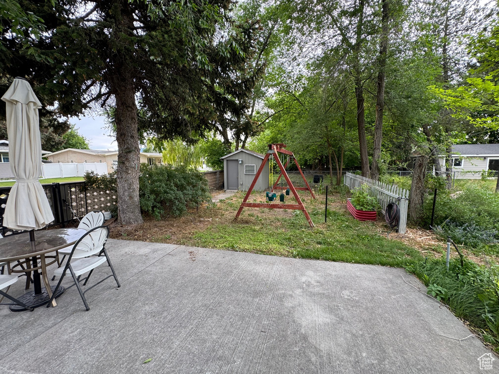 Fenced backyard featuring a patio area, a storage shed, a playground, and outdoor dining space