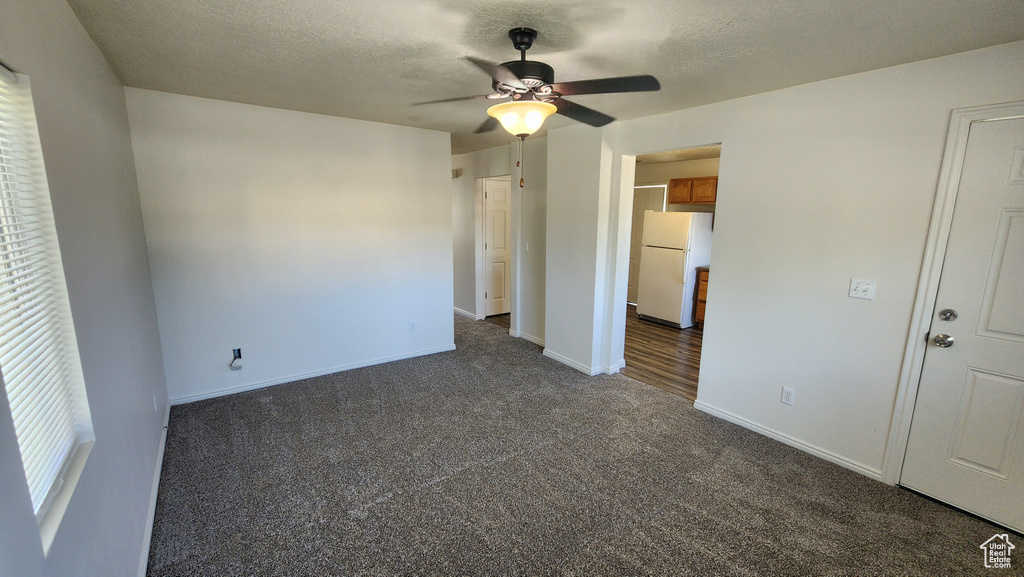 Unfurnished bedroom with freestanding refrigerator, dark carpet, a textured ceiling, and a ceiling fan