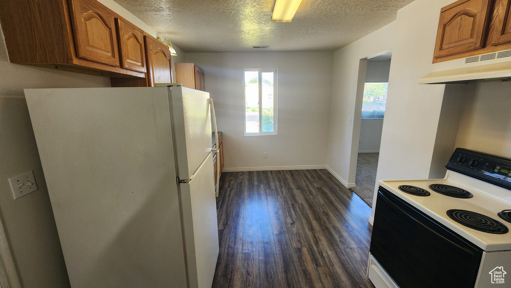 Kitchen with electric stove, freestanding refrigerator, under cabinet range hood, a textured ceiling, and brown cabinetry