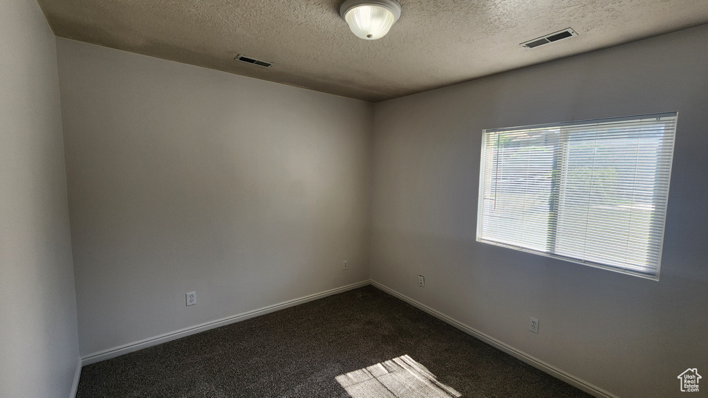 Spare room featuring a textured ceiling and dark colored carpet