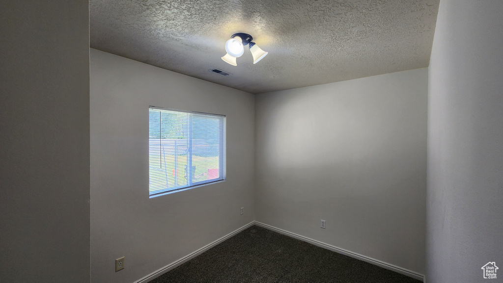 Unfurnished room with a textured ceiling and dark carpet