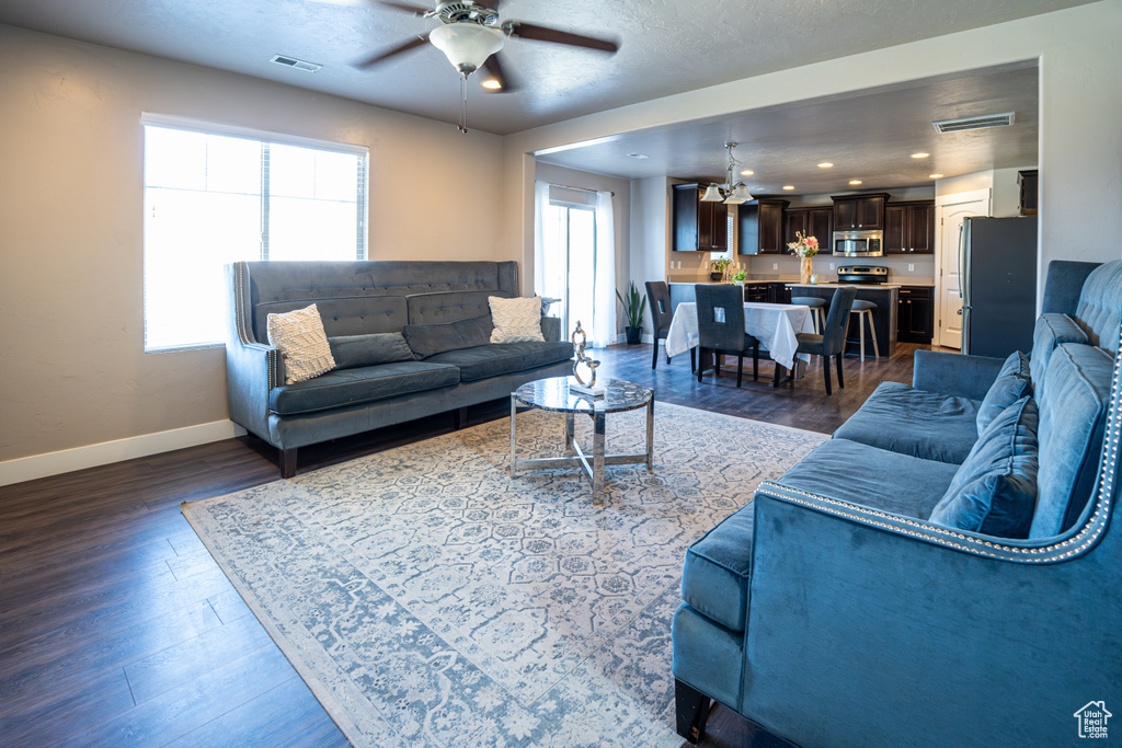 Living area with a chandelier, ceiling fan, and dark wood-style floors