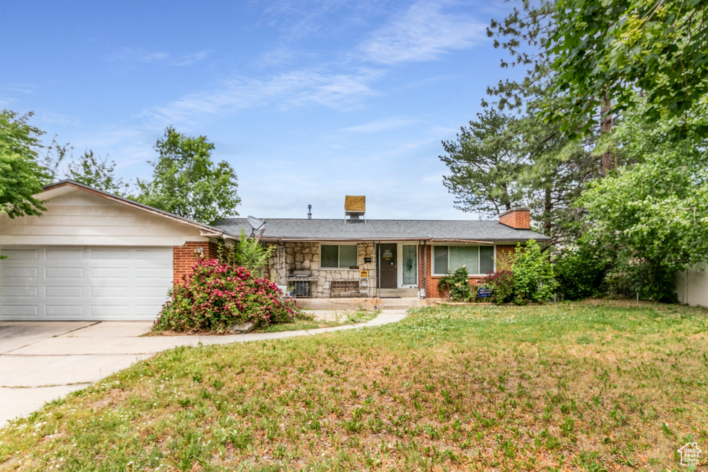 Ranch-style house featuring covered porch, concrete driveway, an attached garage, a chimney, and a front lawn