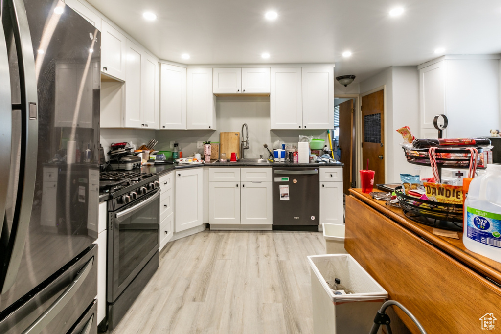 Kitchen with freestanding refrigerator, dishwashing machine, range with gas cooktop, light wood-style flooring, and white cabinets
