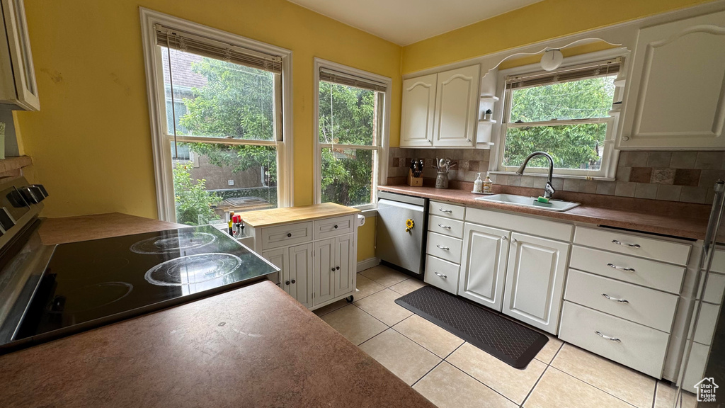 Kitchen featuring dishwasher, electric range, decorative backsplash, light tile patterned floors, and white cabinetry