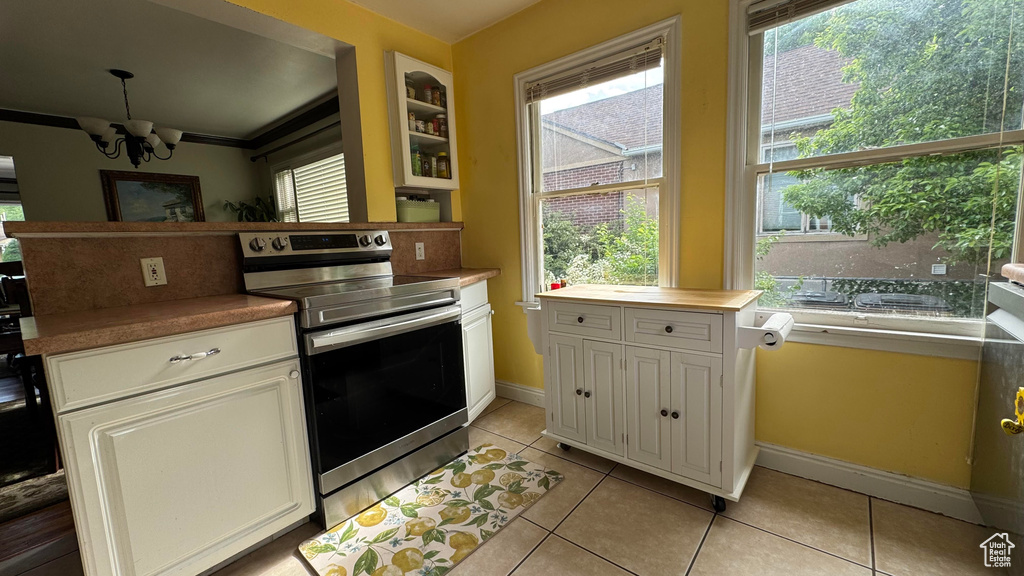 Kitchen featuring electric stove, a chandelier, light tile patterned floors, and white cabinetry