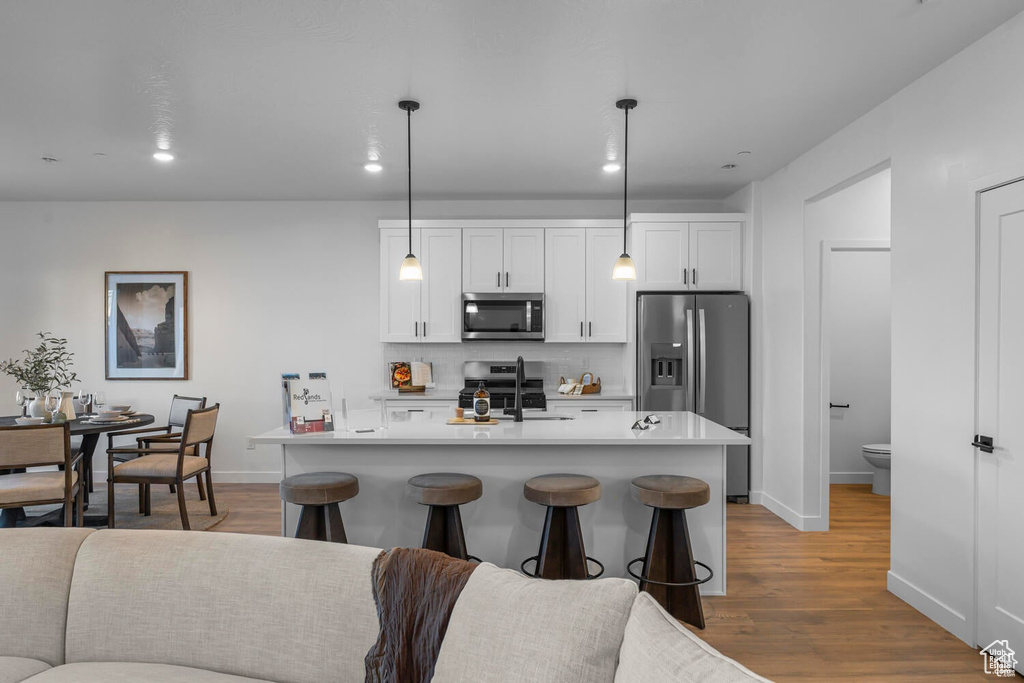 Kitchen with stainless steel appliances, backsplash, light wood finished floors, white cabinetry, and light countertops