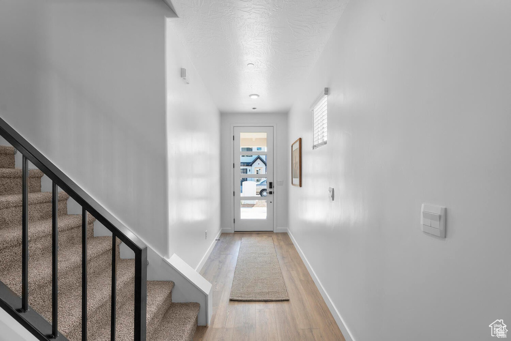 Doorway with light wood finished floors, stairway, and a textured ceiling