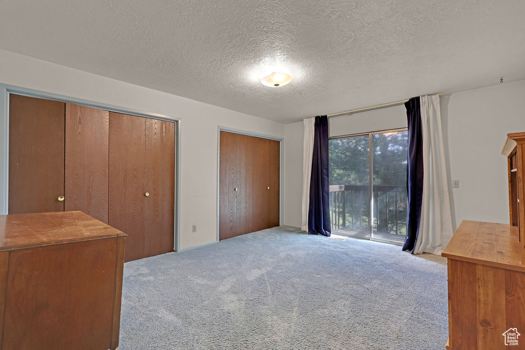 Unfurnished bedroom featuring access to outside, carpet floors, two closets, and a textured ceiling