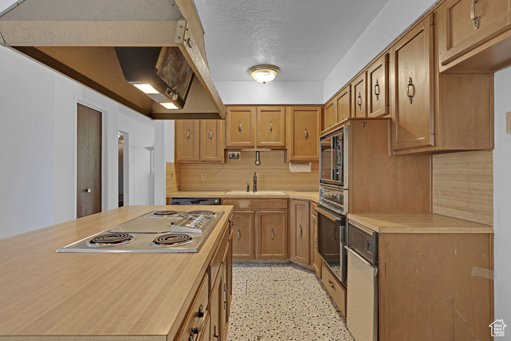 Kitchen with appliances with stainless steel finishes, a textured ceiling, decorative backsplash, dark speckled floor, and brown cabinets