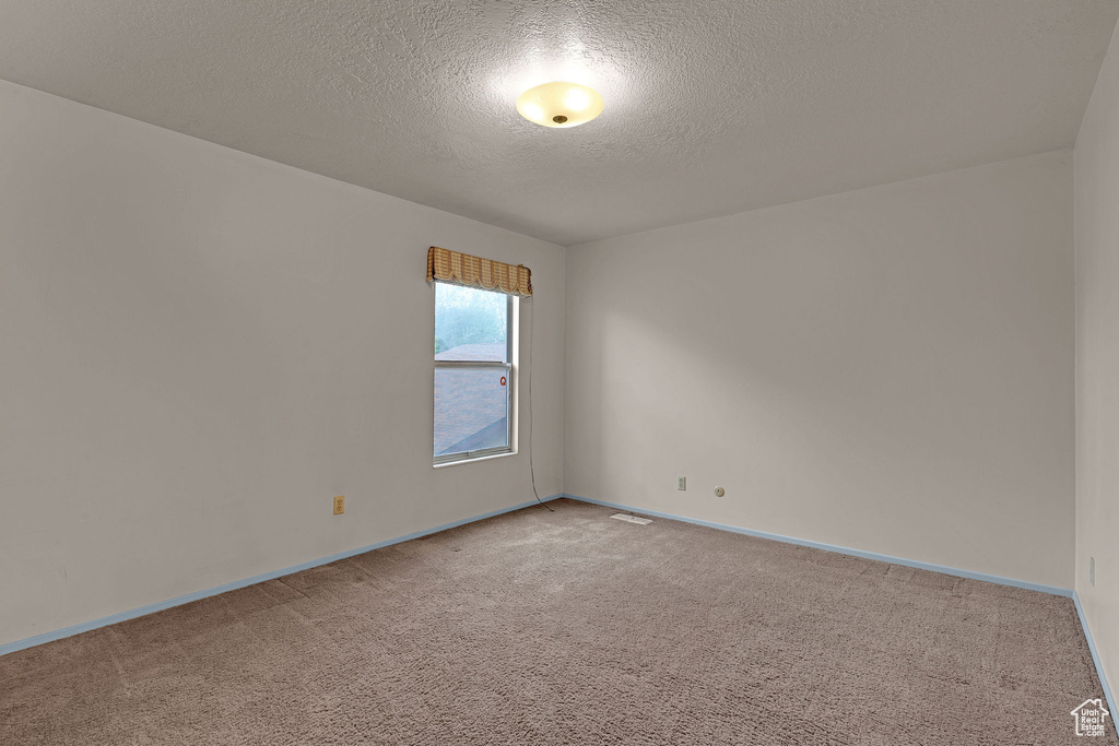 Unfurnished room featuring a textured ceiling and light carpet