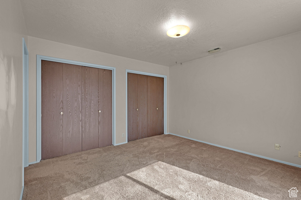 Unfurnished bedroom with carpet, a textured ceiling, and multiple closets