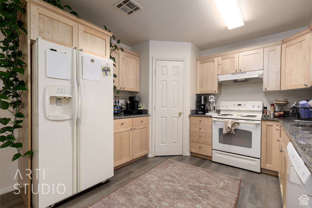 Kitchen featuring white appliances, light brown cabinets, under cabinet range hood, and a textured ceiling