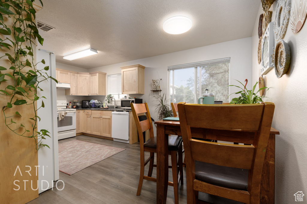 Kitchen featuring white appliances, light brown cabinetry, under cabinet range hood, and wood finished floors