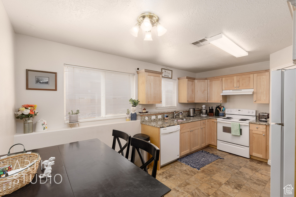 Kitchen featuring white appliances, light brown cabinets, under cabinet range hood, stone finish floors, and a textured ceiling