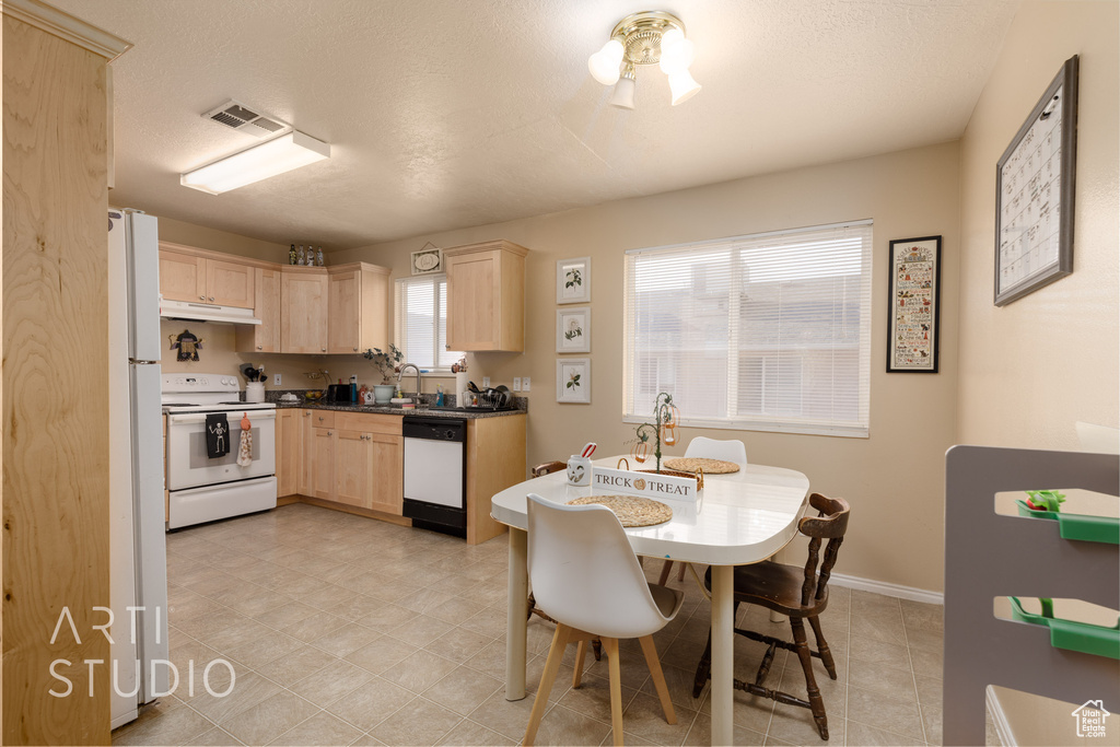 Kitchen with white appliances, light brown cabinets, under cabinet range hood, and dark countertops