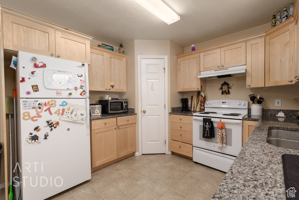 Kitchen with white appliances, light brown cabinetry, and under cabinet range hood