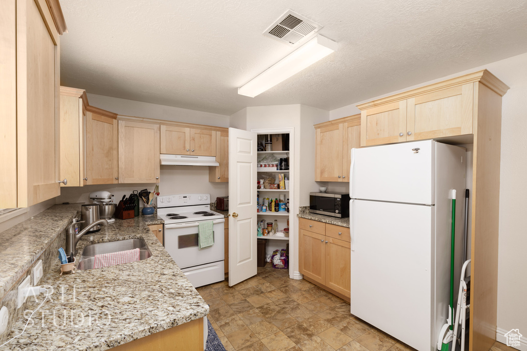 Kitchen featuring white appliances, light brown cabinetry, under cabinet range hood, and light stone counters