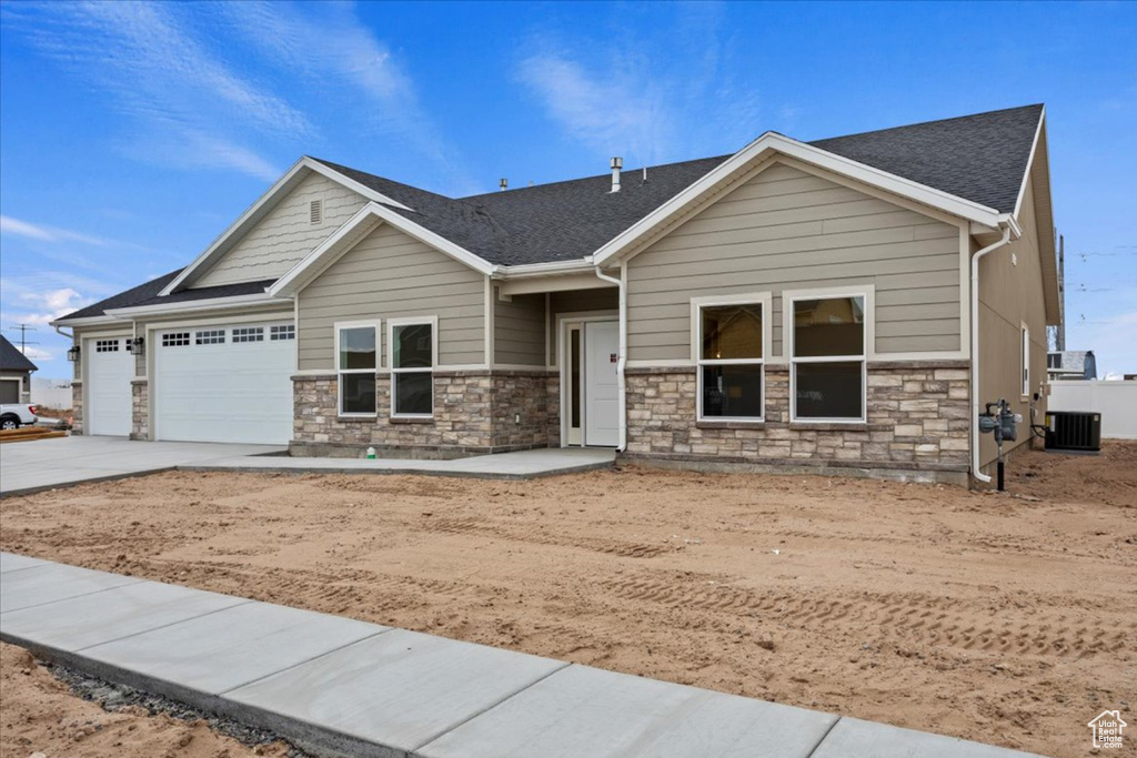 Craftsman house featuring driveway, stone siding, an attached garage, and roof with shingles