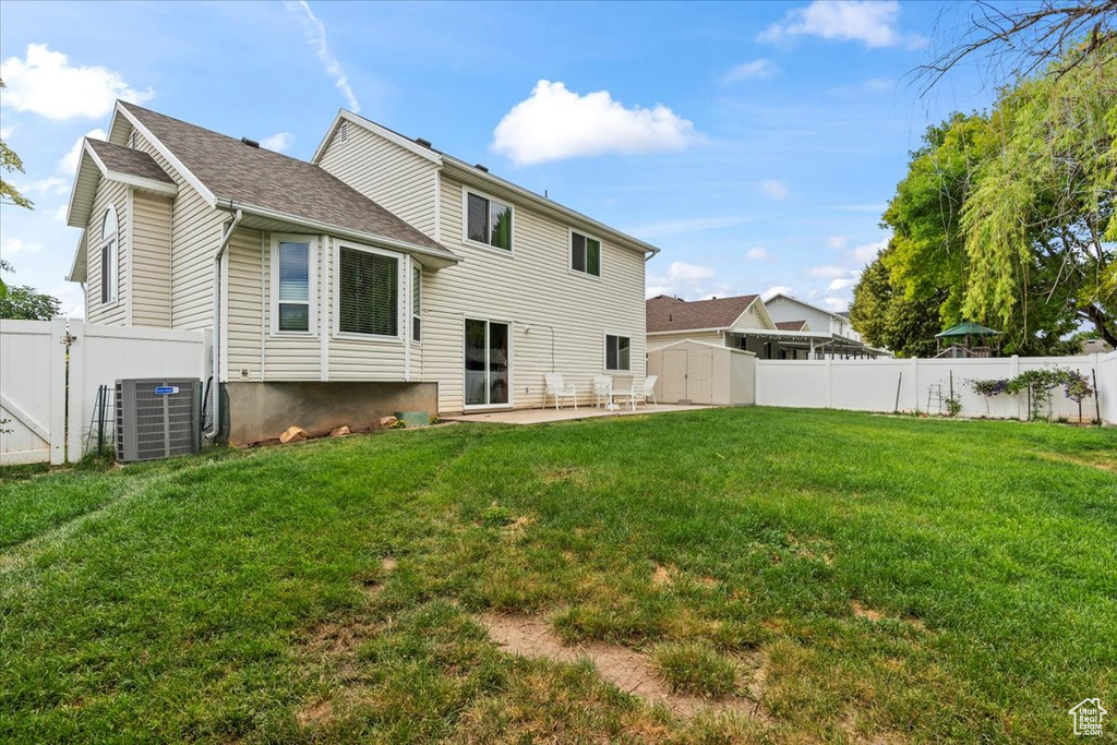 Rear view of property featuring a storage unit, a patio area, a fenced backyard, and roof with shingles
