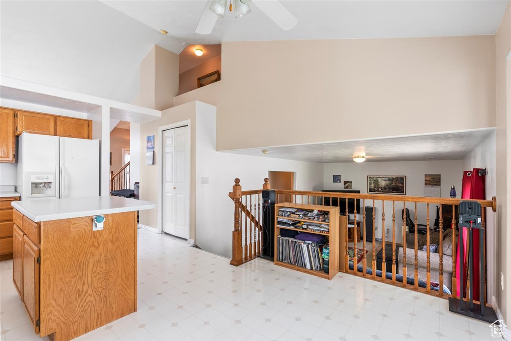Kitchen featuring white fridge with ice dispenser, high vaulted ceiling, light floors, light countertops, and a center island