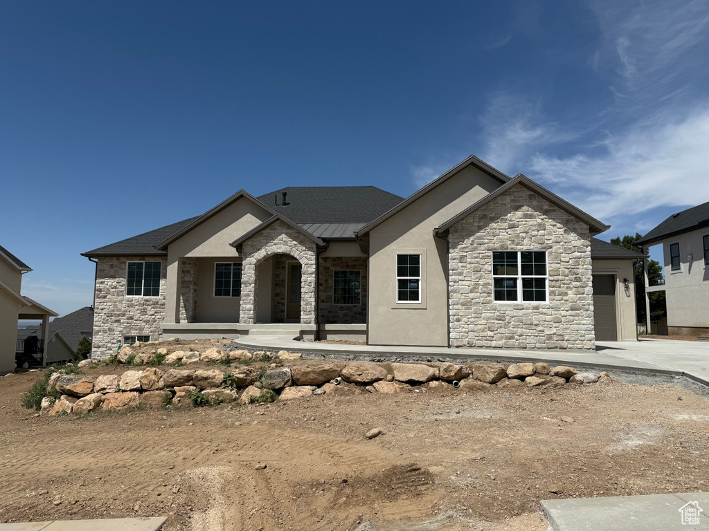 View of front facade with stone siding, a standing seam roof, a garage, driveway, and a metal roof