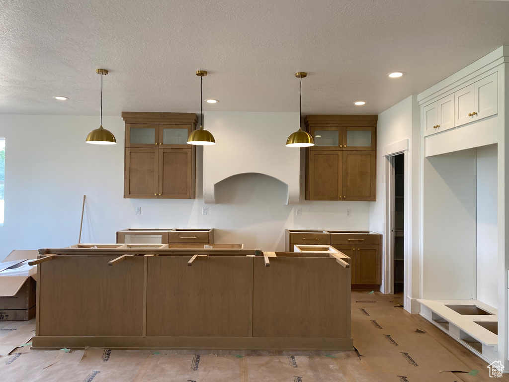 Kitchen with brown cabinetry, glass insert cabinets, a center island, pendant lighting, and recessed lighting