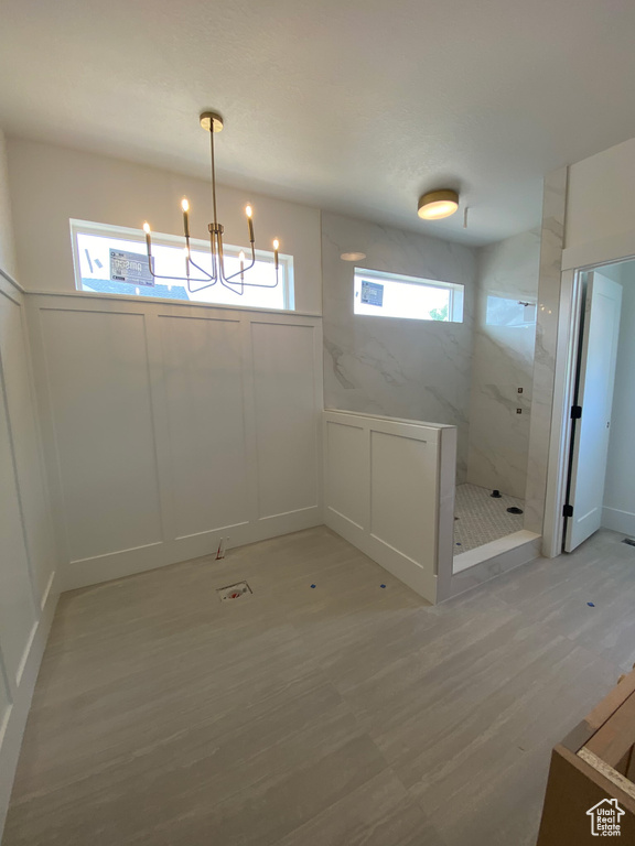 Unfurnished dining area with a decorative wall, plenty of natural light, a chandelier, light wood-type flooring, and a wainscoted wall