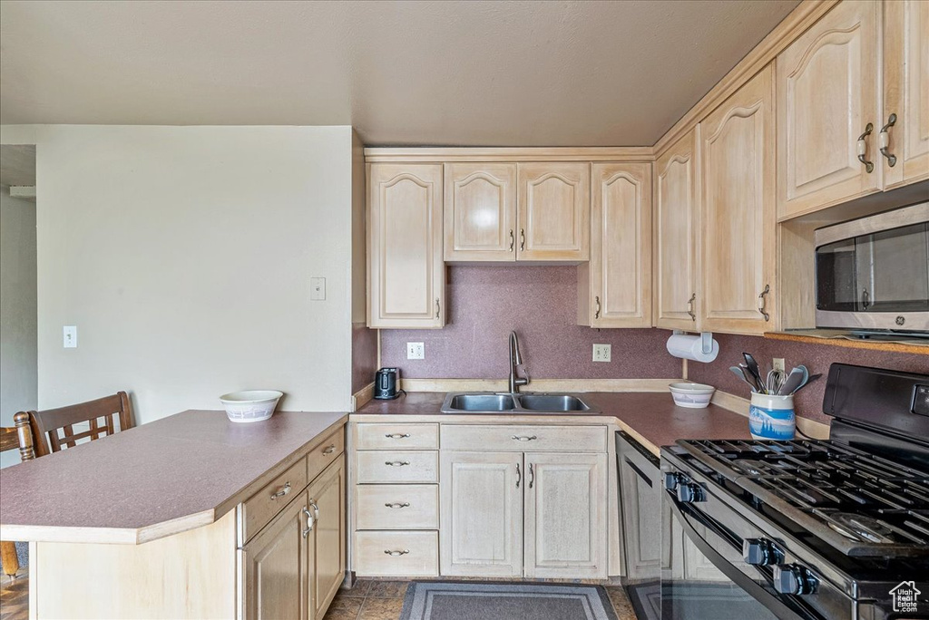 Kitchen with gas stove, stainless steel microwave, light brown cabinetry, and a peninsula