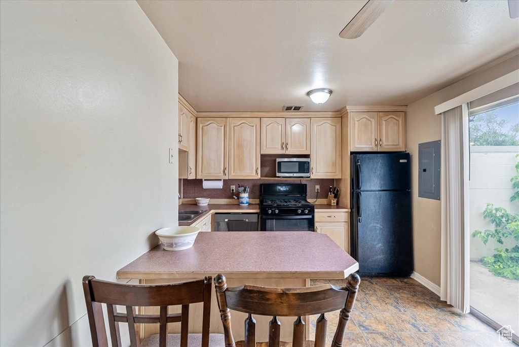 Kitchen featuring black appliances, electric panel, light brown cabinets, light stone finish floors, and light countertops