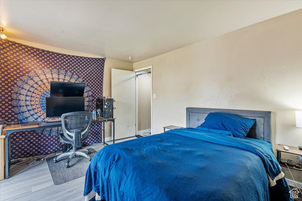 Bedroom with wood finished floors, wallpapered walls, and an accent wall