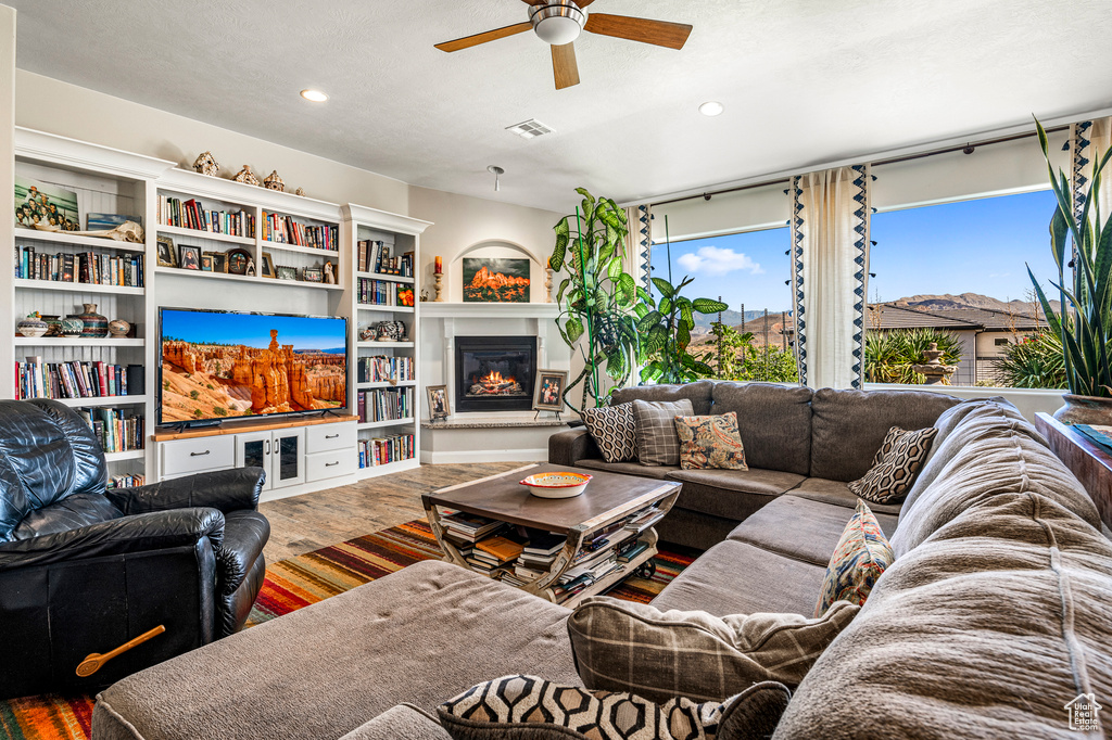 Living room with a ceiling fan, a glass covered fireplace, recessed lighting, and wood finished floors
