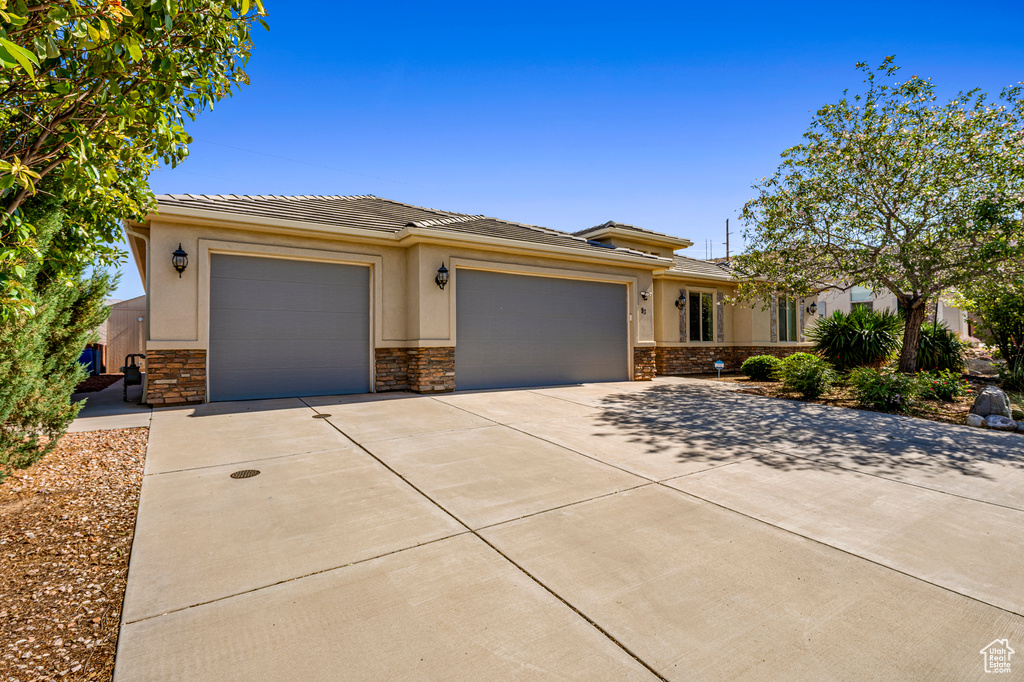 Prairie-style home with a garage, driveway, stone siding, a tile roof, and stucco siding