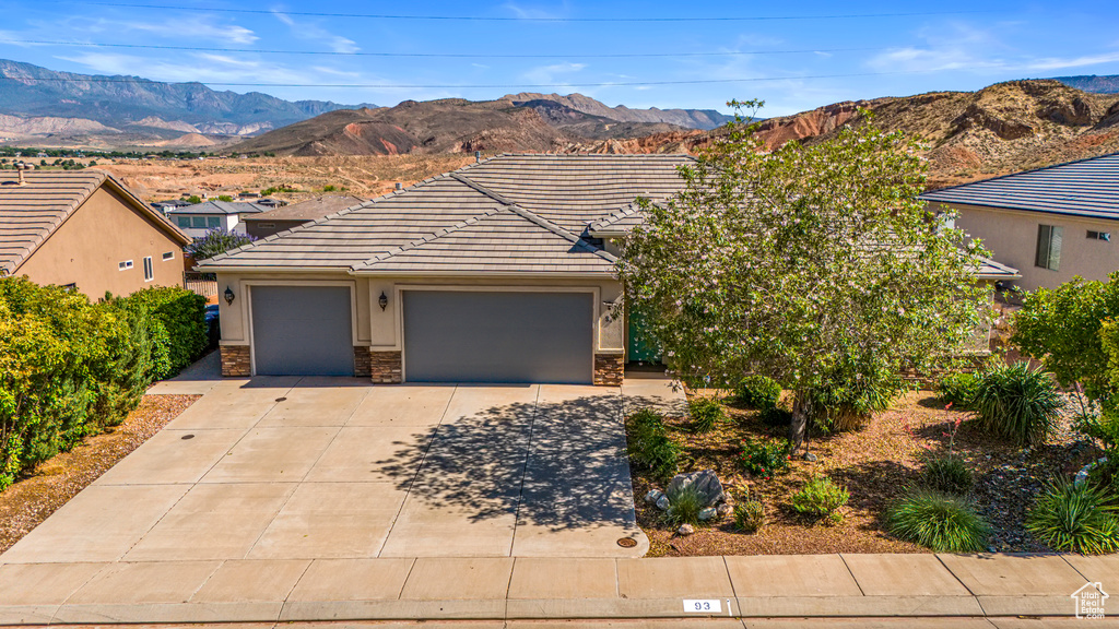 View of front of house featuring driveway, a tile roof, an attached garage, stone siding, and a mountain view