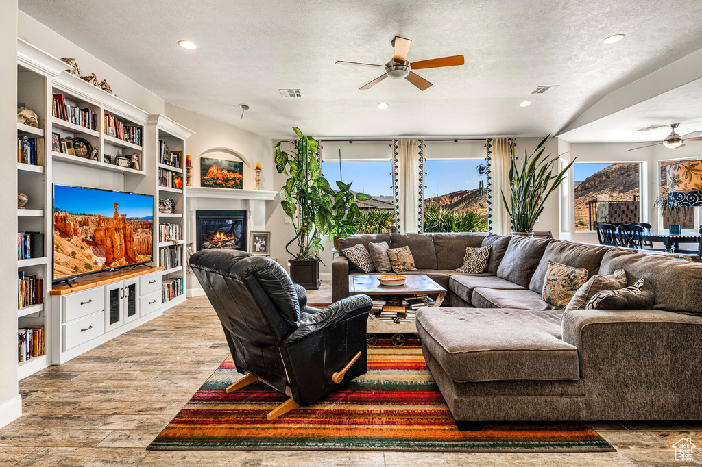 Living area featuring ceiling fan, wood finished floors, recessed lighting, a glass covered fireplace, and built in features