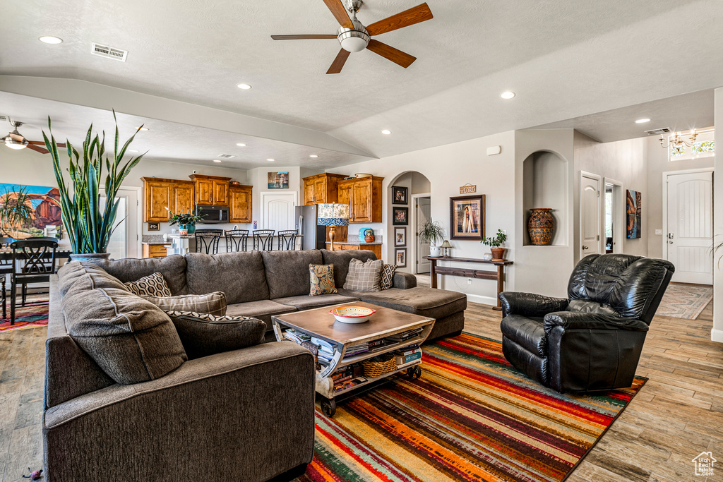 Living area with ceiling fan, vaulted ceiling, arched walkways, light wood-style floors, and recessed lighting