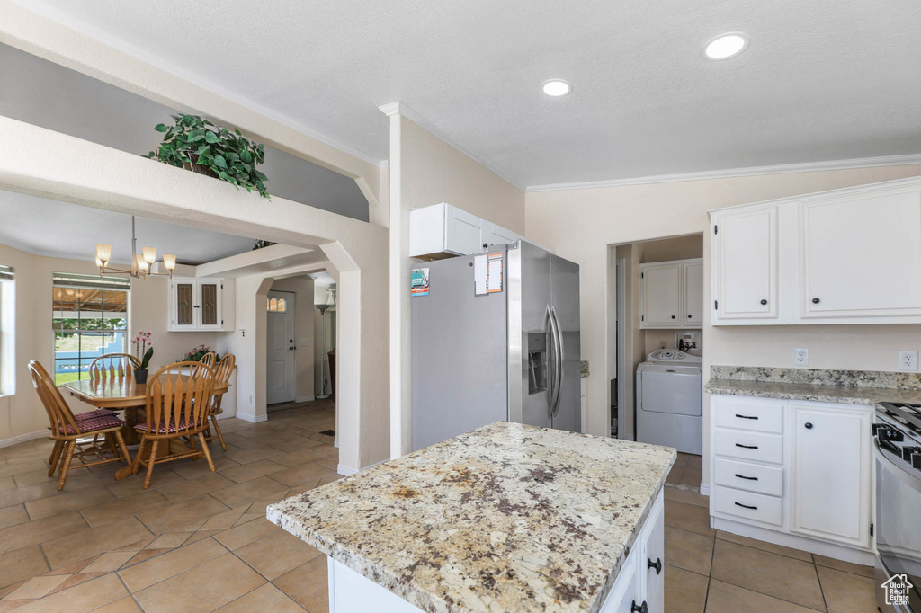 Kitchen featuring stainless steel fridge, washer / dryer, white cabinets, arched walkways, and gas range oven
