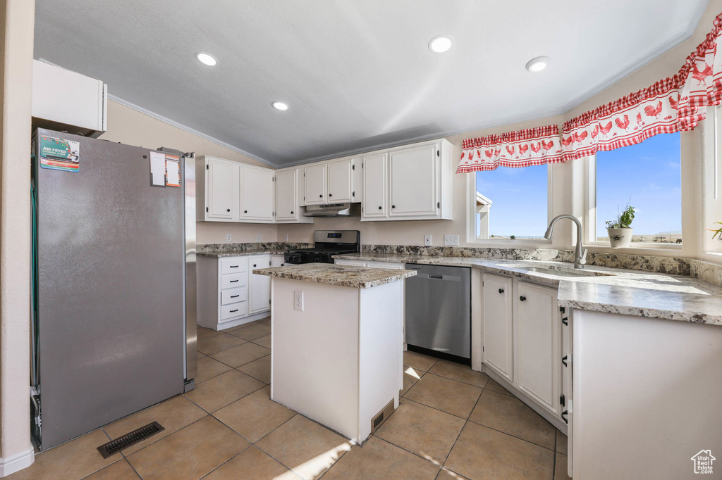 Kitchen featuring appliances with stainless steel finishes, under cabinet range hood, vaulted ceiling, white cabinets, and a center island