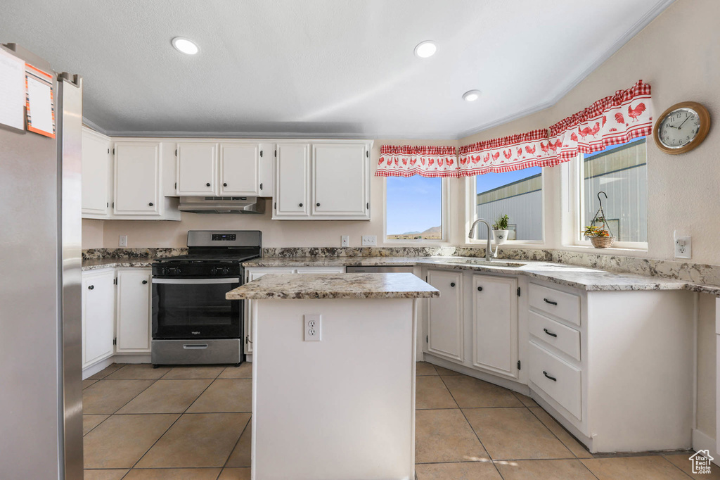 Kitchen with stainless steel appliances, under cabinet range hood, white cabinets, light tile patterned flooring, and a kitchen island