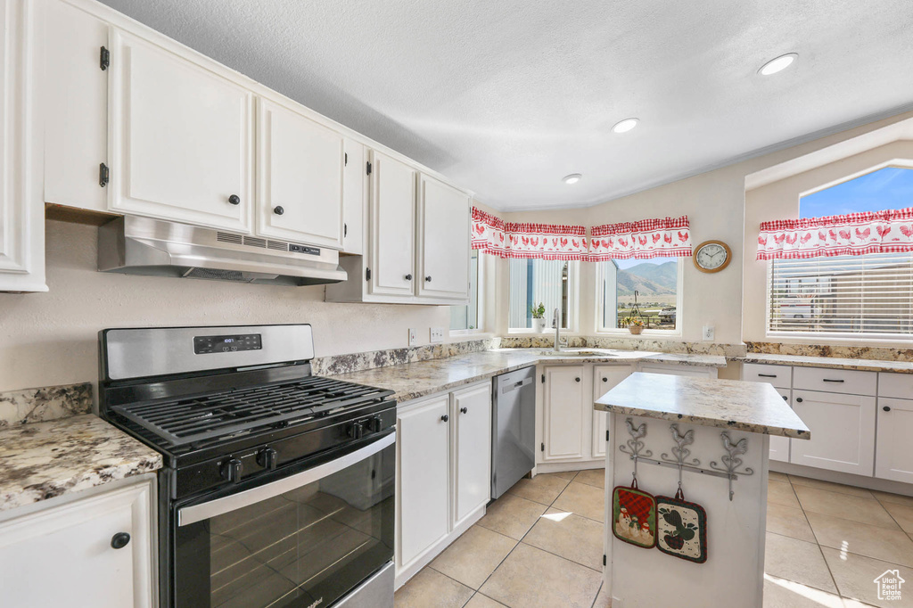 Kitchen featuring appliances with stainless steel finishes, under cabinet range hood, white cabinets, a center island, and light tile patterned floors