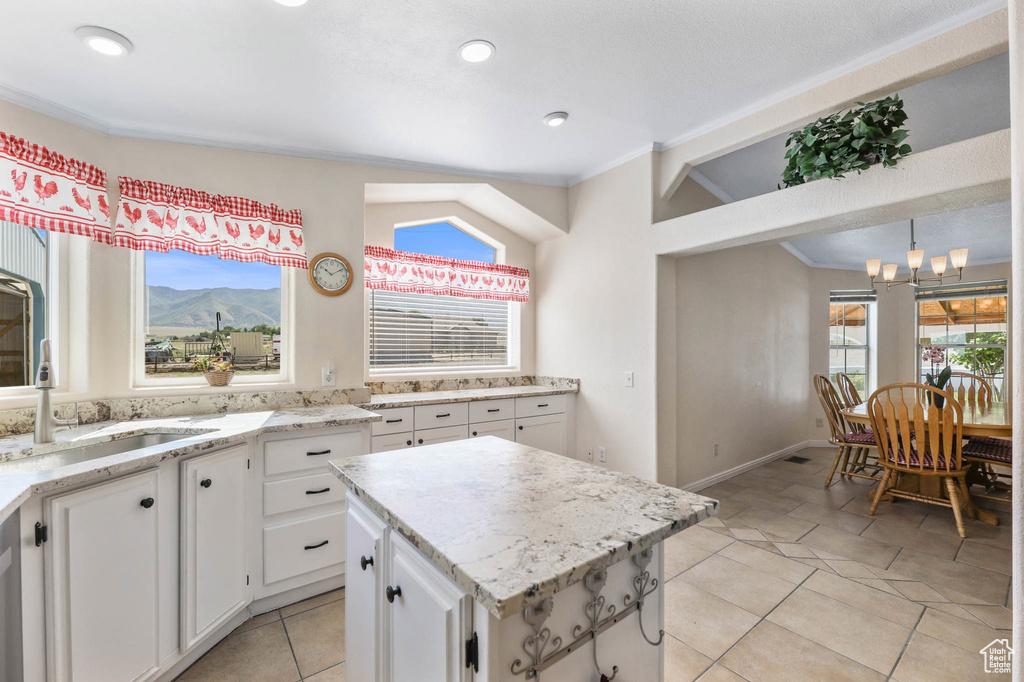 Kitchen with a chandelier, light tile patterned floors, white cabinetry, a kitchen island, and ornamental molding