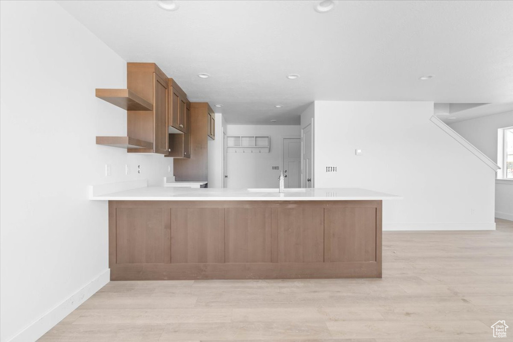 Kitchen with a peninsula, light wood-type flooring, open shelves, light countertops, and recessed lighting