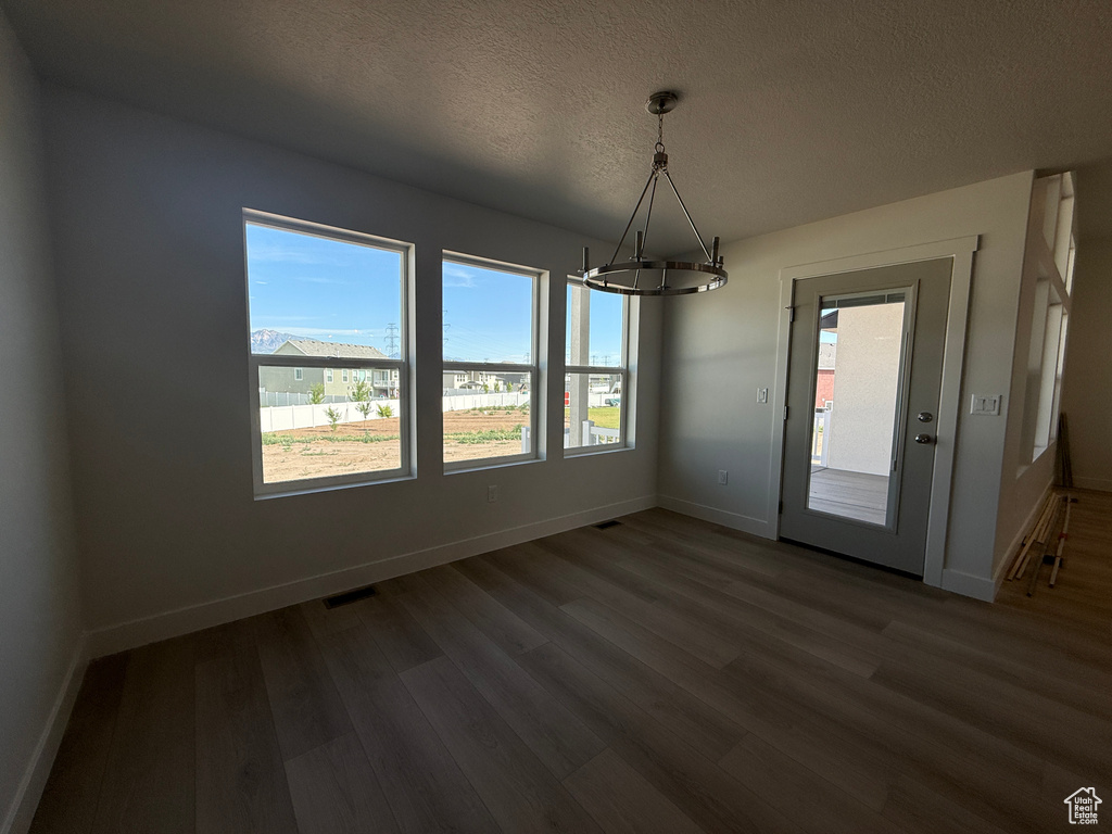 Unfurnished dining area with a chandelier, dark wood-style flooring, plenty of natural light, and a textured ceiling