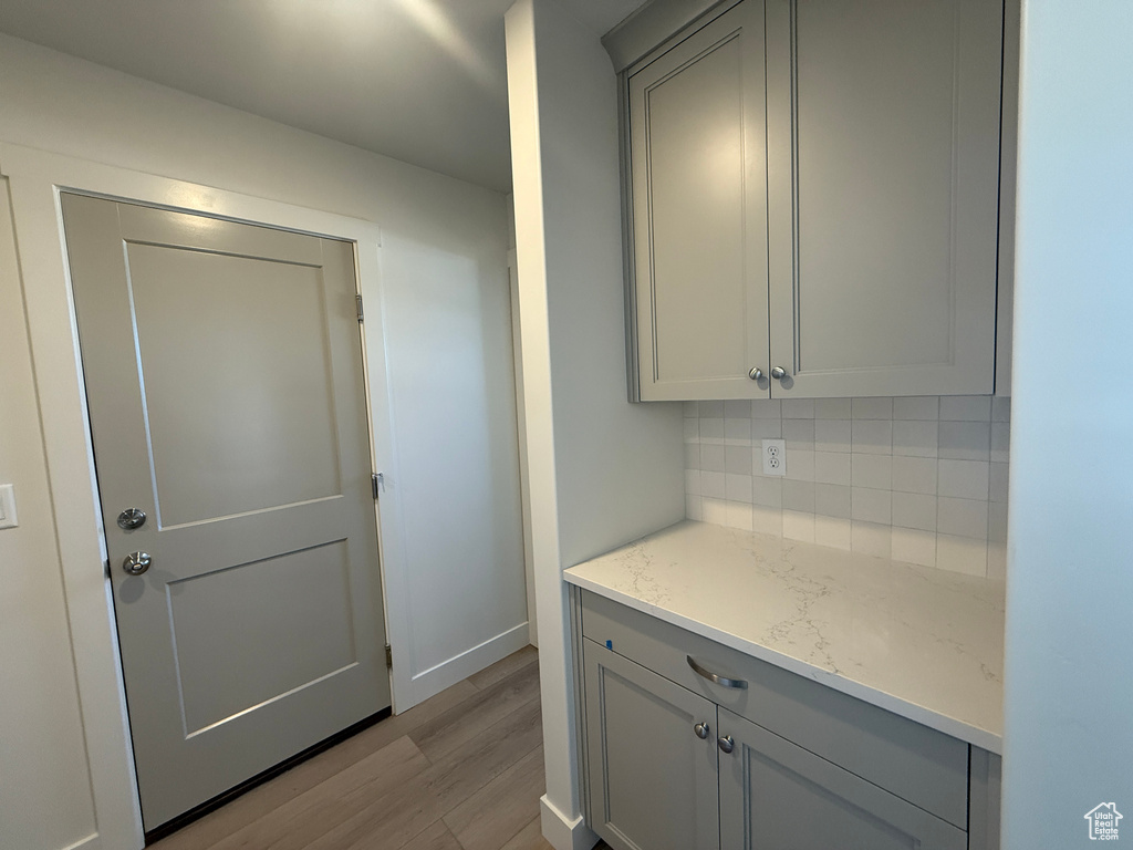 Kitchen with gray cabinetry, decorative backsplash, wood finished floors, and light stone countertops