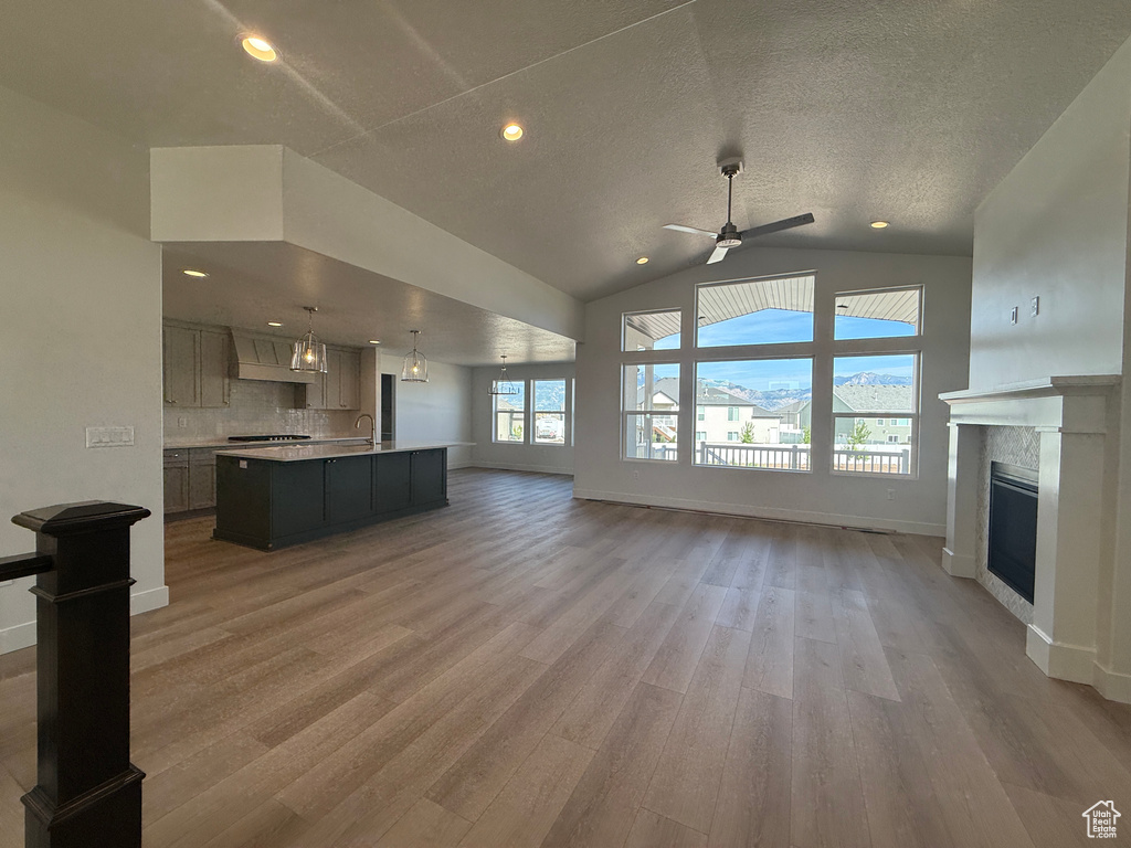 Unfurnished living room featuring a fireplace, light wood-style floors, ceiling fan, vaulted ceiling, and a textured ceiling