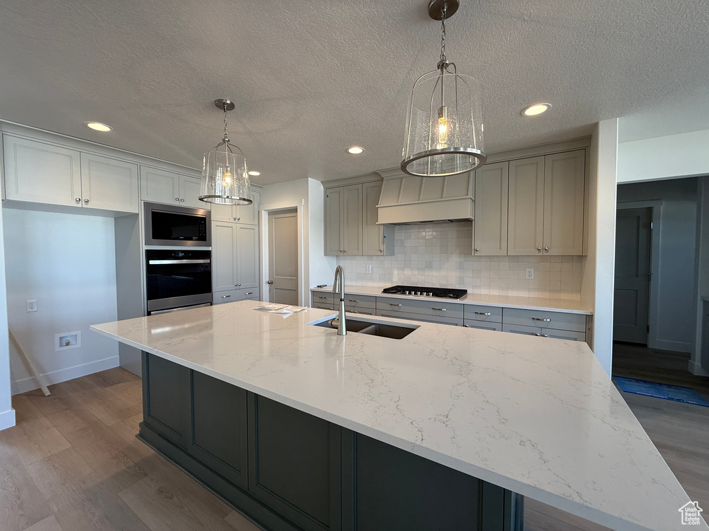 Kitchen featuring appliances with stainless steel finishes, dark wood-style floors, backsplash, a textured ceiling, and a large island with sink