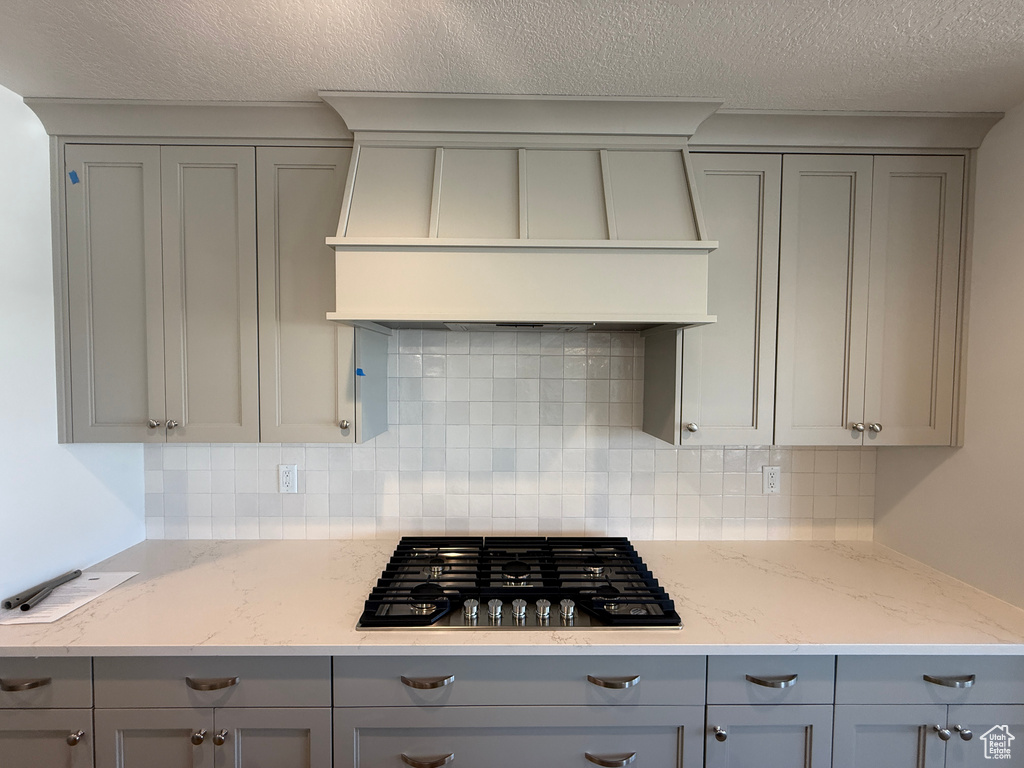 Kitchen with gray cabinetry, gas stovetop, custom range hood, and a textured ceiling