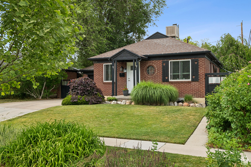 Bungalow-style house with brick siding, a front yard, a chimney, roof with shingles, and concrete driveway