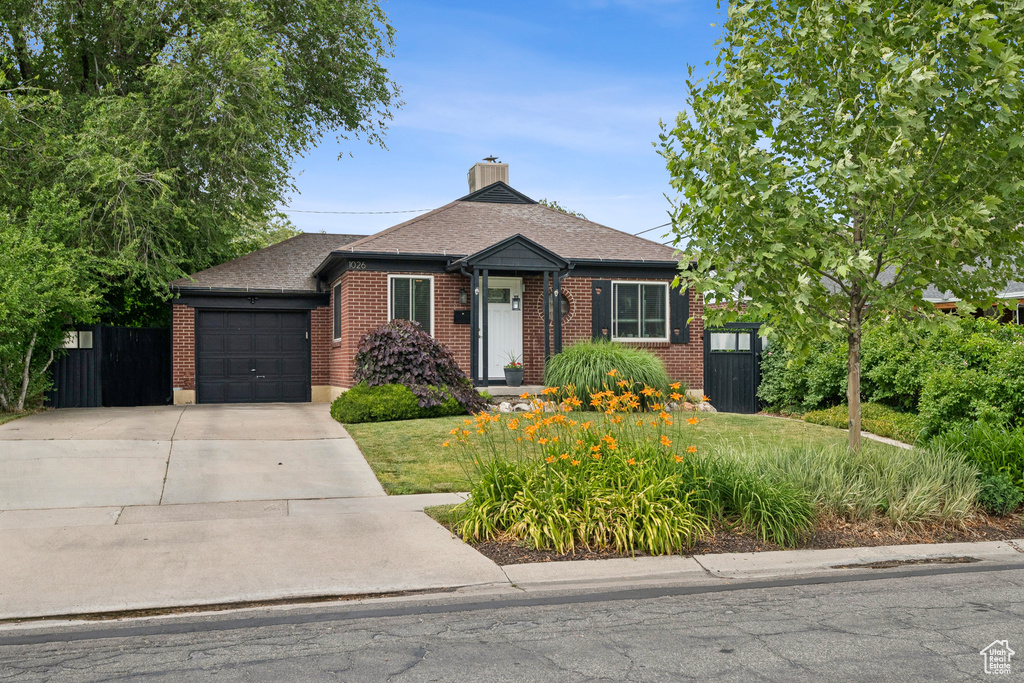 View of front of house with an attached garage, driveway, brick siding, a shingled roof, and a chimney