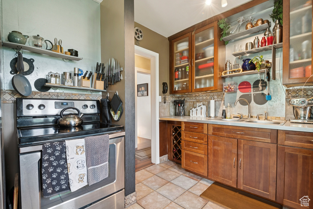 Kitchen featuring stainless steel electric range oven, backsplash, open shelves, light tile patterned flooring, and light countertops